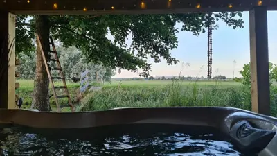 a bath tub with a view of a tree and a ladder at Wellness Lodge aan de Braassem in Rijnsaterwoude