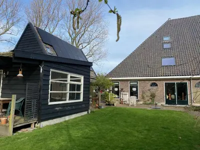 a black house with a pitched roof and a yard at Holidayhome Geuzenhoeve op de Munnickaij in Schellinkhout