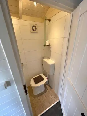 a small bathroom with a toilet with a wooden floor at Pipowagen aan zee in Bergen aan Zee