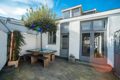 a patio with a wooden bench and a tree at Sandy's Family Beach House for 2 adults & 2 children in Zandvoort