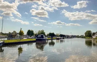 a boat is docked in a river with clouds in the sky at Holiday Home Breukelen Iv in Breukelen