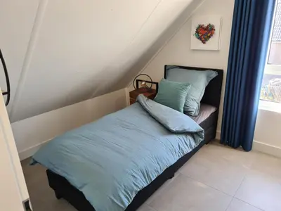 a bedroom with a bed with blue sheets and a window at Bungalow 76 op Recreatiepark de Wielen in Sint Maarten