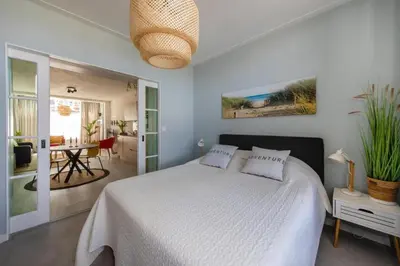 a bedroom with a white bed and a dining room at Nina's Beach House 2 
