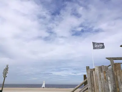 a flag on the beach with a sailboat in the ocean at Ferienhaus-Naumann-Kreetz in Burgerbrug
