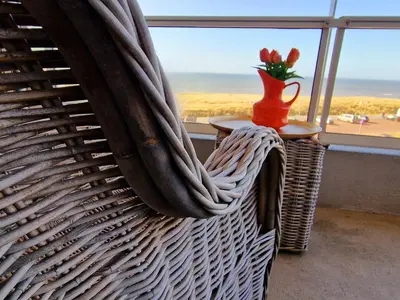 a wicker chair with a vase on a table and a window at Studio Noordzee in Egmond aan Zee