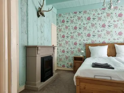 a bedroom with a bed with a fireplace and floral wallpaper at Het Voorhuis boerderij Hoeve Vrede Best in Weesp