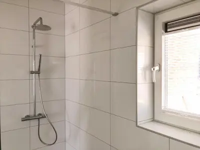 a shower in a bathroom with white tiles at Bungalow 74 op Recreatiepark De Wielen in Sint Maarten