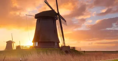 a windmill on a hill with a sunset in the background at Buitenliefde, romantisch verblijf voor 2 personen in Heiloo