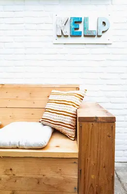 a wooden bench with two pillows and a sign on a wall at Kelp in Egmond aan Zee