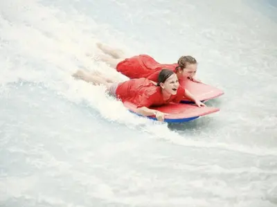 two people riding on a surfboard in the water at Green Tiny House with shared pool in Zeewolde
