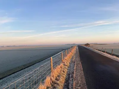 a road next to a fence next to the water at Stylish holiday home by the sea in Tuitjenhorn