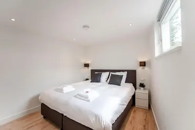 a bedroom with a bed with white sheets and a window at Happy Days Apartment - Luxurious - Free parking on own property in Zandvoort