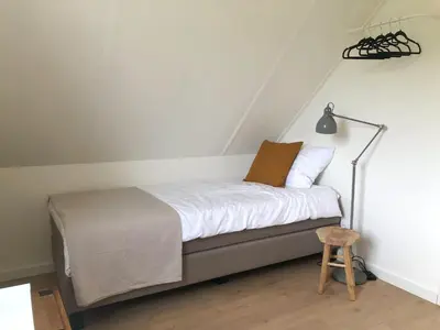 a bedroom with a bed with white sheets and a stool at Bungalow 82 op Recreatiepark De Wielen in Sint Maarten
