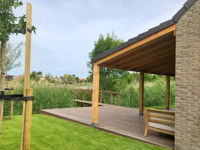 a wooden deck with a bench on the grass at Bungalow 82 op Recreatiepark De Wielen in Sint Maarten