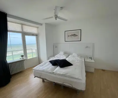 a white bedroom with a bed and a large window at Zwarte Vis in Zandvoort