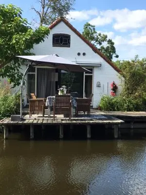a house with a table and chairs on a dock next to the water at De Beijersche Stee , Landhuysje in Stolwijk