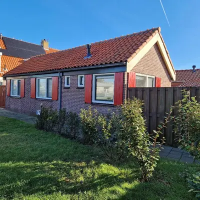 a house with red windows and a fence at Het Zomerhuis in Egmond-Binnen