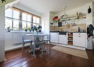a kitchen with white cabinets and a table and chairs at Idyllisch en knus huisje met prachtige veranda. in Oterleek