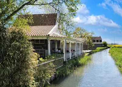 a house on the side of a river at Idyllisch en knus huisje met prachtige veranda. in Oterleek