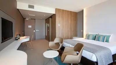 a hotel room with a bed and chairs and a tv at Strandhotel Golfzang in Egmond aan Zee