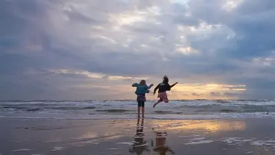 a man and a girl jumping on the beach at Molecaten Park Noordduinen in Katwijk