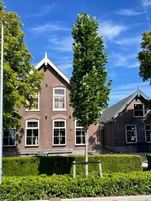 a large brick house with a tree in front of it at trendy boutique appartement vlak bij Amsterdam in Rijnsaterwoude