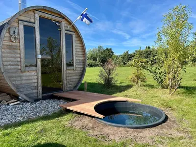 a round wooden hobbit house with a wooden deck and a pond at Stuga Kodawari in Voorhout