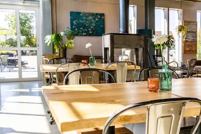 a restaurant with wooden tables and chairs and windows at Vakantiepark Koningshof in Rijnsburg