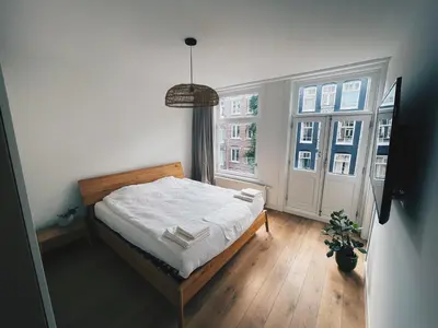 a small bedroom with a bed and two windows at Spacious Designer Duplex next to Central Park in Amsterdam