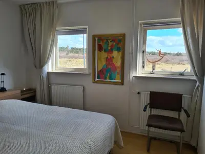 a bedroom with a bed and two windows and a chair at appartement Ideaal in Bergen aan Zee
