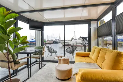 a living room with a yellow couch and a table and chairs at Cosy tiny houseboats near beach and restaurants by Weltevreden Experience in Zeewolde