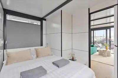 a bedroom with a white bed with a window at Cosy tiny houseboats near beach and restaurants by Weltevreden Experience in Zeewolde