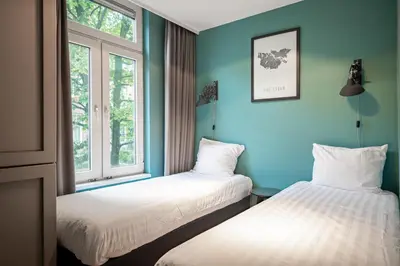 two beds in a room with blue walls and windows at Musea Hotel & Apartments in Amsterdam