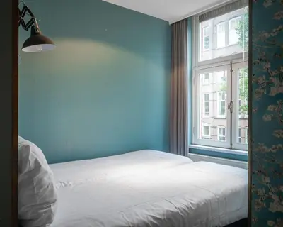 a blue bedroom with a bed and a window at Musea Hotel & Apartments in Amsterdam