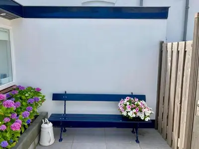 a blue bench sitting next to a white wall with flowers at Have a nice stay! - Beachhouse Stranddistel 100m from the beach in Noordwijk aan Zee