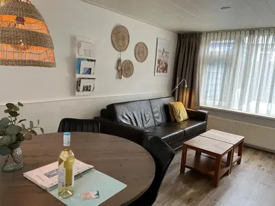 a living room with a black leather couch and a table at Zomerhuis Beach EnJoy in Egmond aan Zee
