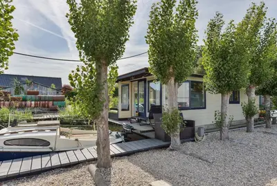 a house with a boat in a yard with trees at Woonark Westeinder with kayaks close to Schiphol Airport in Aalsmeer