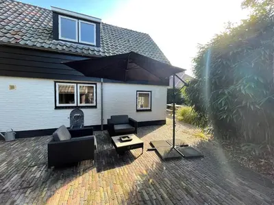 a patio with furniture and an umbrella in front of a house at Bergense Duyn by Droomvilla in Bergen