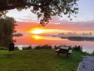 a bench sitting next to a lake at sunset at Walvisch van Ghyspe in Wormer