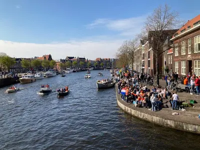 a group of people sitting on the side of a river with boats at GuesthouseOne in Haarlem