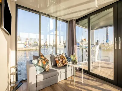 a living room with a couch and large windows at Beautiful houseboat with shared pool in Volendam