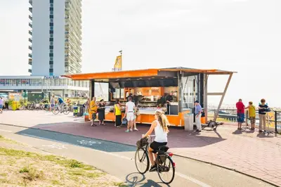 a woman riding a bike in front of a food truck at CHALET FOR 2 AT THE BEACH in Zandvoort