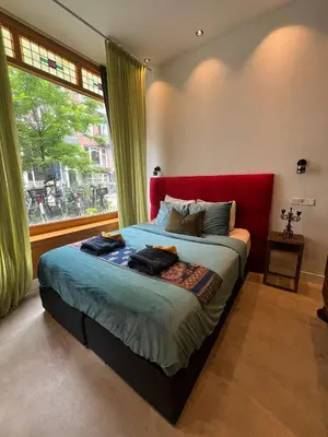 a bedroom with a bed with a red headboard and a window at Boutique Amsterdam Homestay in Amsterdam
