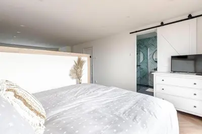 a white bedroom with a bed and a tv at Windhoek Apartment in Zandvoort