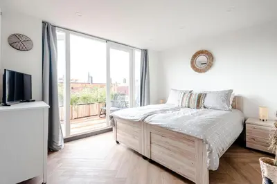 a white bedroom with a bed and a large window at Windhoek Apartment in Zandvoort