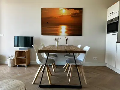 a dining room with a wooden table and white chairs at Dunefront Apartment in Zandvoort