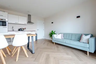 a living room with a blue couch and a kitchen at Dunefront Apartment in Zandvoort