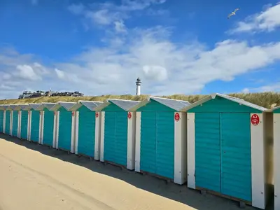a row of blue and white beach huts on a beach at De Witte Vos in Egmond aan Zee
