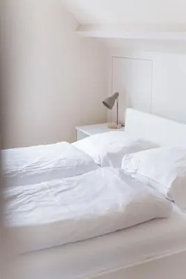 a white bedroom with two white beds and a lamp at - Het Kleine Nest - nabij het meer, strand & Keukenhof in Noordwijkerhout