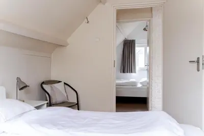 a bedroom with a bed and a chair and a mirror at - Het Kleine Nest - nabij het meer, strand & Keukenhof in Noordwijkerhout